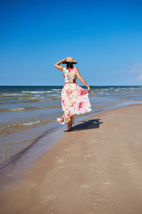 Obraz na płótnie Canvas A relaxed girl with a hat goes along the beach.