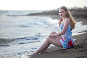 Fototapeta na wymiar Beautiful girl sits on a sandy beach on the seashore