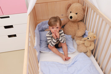 Ein zweijähriger Junge sitzt weinend in seinem Kinderbett - obrazy, fototapety, plakaty