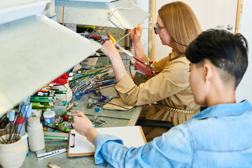 High angle portrait of two young women melting glass over gas torch while making handmade beads in modern creative workshop, copy space