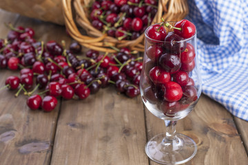 A large basket of ripe cherries and scattered berries on a table and in a glass. Wooden background, free space for text. Retro style. Copy space