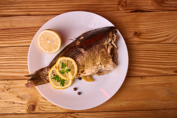 Grilled fish with herbs and lemon on wooden background. Mediterranean luxurious seafood concept