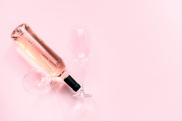 Bottle of pink wine and two glasses of wine on a soft light pink wood table, mock up. Flat lay, top view, copy space 