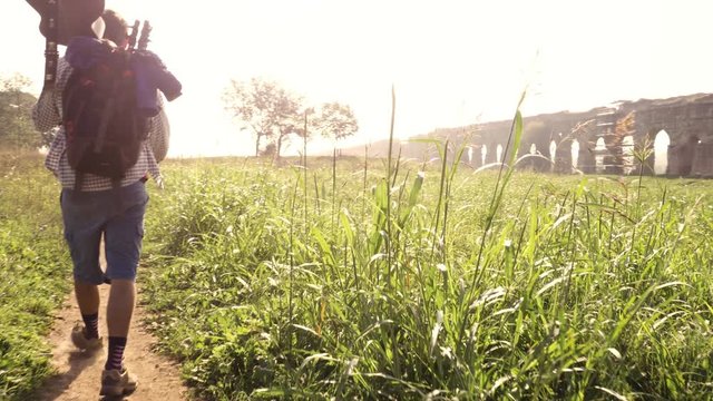 Young couple backpackers tourists walking near roman aqueduct arches in parco degli acquedotti park ruins in rome at sunrise with guitar and sleeping bag slow motion steadycam