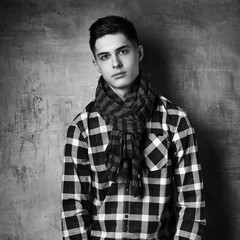 Obraz premium Portrait of young trendy handsome man with short dark hair wearing checkered shirt and brown trousers standing and posing against gray concrete wall