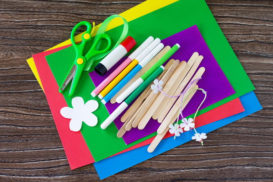 Colored paper, glue, sheets, ribbons, flowers for making a gift summer flowers on wooden sticks fence. Handmade. Project of children's creativity, handicrafts, crafts for kids.