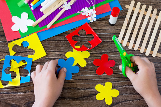 A child is cutting details of a gift of summer flowers on a wooden sticks fence. Handmade. Project of children's creativity, handicrafts, crafts for kids.