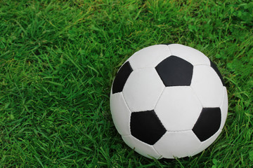 Fototapeta na wymiar Football black and white ball on the green grass, top view.