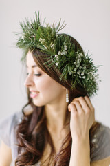 Portrait of pretty young girl in a gray evening dress and a wreath of pine and eucalyptus on her head. Bridesmade poses in the studio before wedding ceremony.