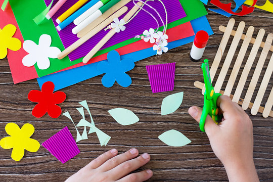A child is cutting details of a gift of summer flowers on a wooden sticks fence. Handmade. Project of children's creativity, handicrafts, crafts for kids.
