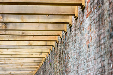 Heavy wooden beams of a newly constructed pergola attached to the brick wall of a walled garden.