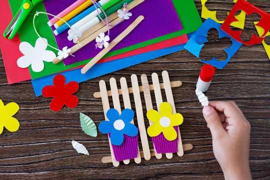 The child folds the origami details of the gift of summer flowers on wooden sticks fence. Handmade. Project of children's creativity, handicrafts, crafts for kids.