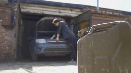 Canister stands in front of young man repairs car in garage