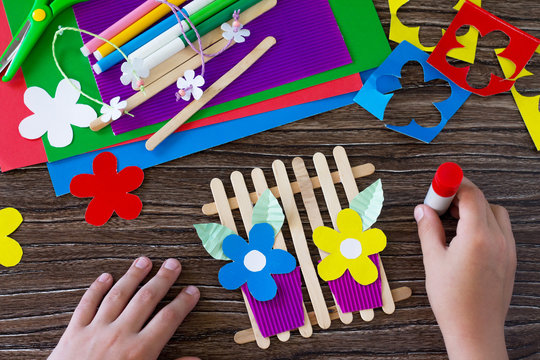 The child glues the details of the gift of summer flowers on wooden sticks fence. Handmade. Project of children's creativity, handicrafts, crafts for kids.