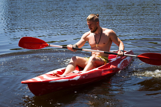 Young Guy Athlete On A Red Kayak With An Oar