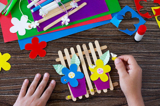 The child glues the details of the gift of summer flowers on wooden sticks fence. Handmade. Project of children's creativity, handicrafts, crafts for kids.