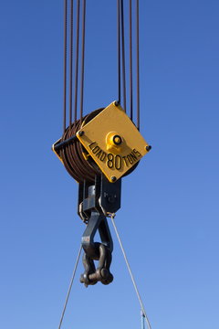 Close up image of a steel cable pulley on  a crane against a blue sky.