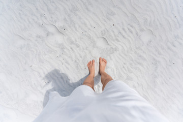 Young woman looking down pov point of view perspective on bare feet standing in white sand in Fort Walton Beach, Florida, in white dress, flat top view with shadow - obrazy, fototapety, plakaty