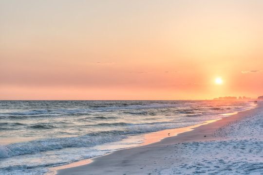 Dreamy pink peach orange sunset in Santa Rosa Beach, Florida with Pensacola coastline coast cityscape skyline in panhandle with ocean gulf mexico waves, birds
