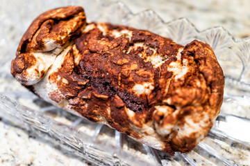 Golden brown baked whole cinnamon roll cake, or babka pastry bread in crystal glass dish on table for festive traditional holiday