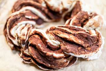 Braided closeup of golden red orange baked whole cinnamon roll swirl twist spiral cake bread on parchment paper tray for festive traditional holiday