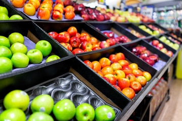 Many varieties assorted red apples on display shelf in grocery store boxes in aisle, supermarket...