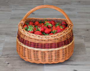 Fototapeta na wymiar Wicker basket full of ripe garden strawberries on grey / brown wooden tiles. Fresh home grown strawberry in basket.
