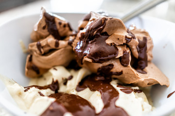 Soft serve vanilla and chocolate ice cream with dark brown syrup drizzled sauce macro closeup in white bowl with spoon