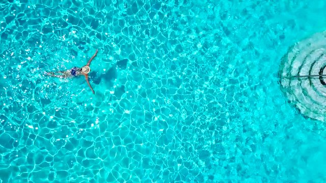 View from the top as a woman in a blue swimsuit swims in the pool