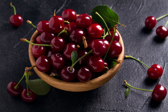 Fresh cherry in wooden bowl on black background. Fresh ripe sweet cherries
