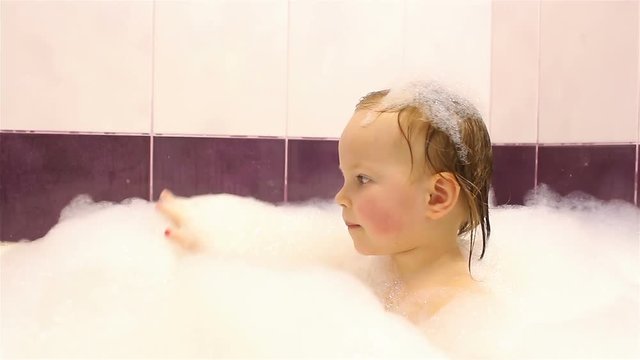 little happy girl bathes in the bathroom with foam. He plays with foam.