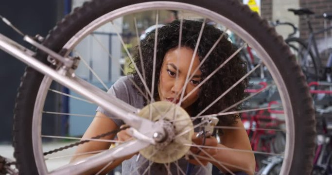 Close up of young Black woman working on bicycle in alley behind bike shop, Attractive African American repair worker tightening derailleur on bike, 4k