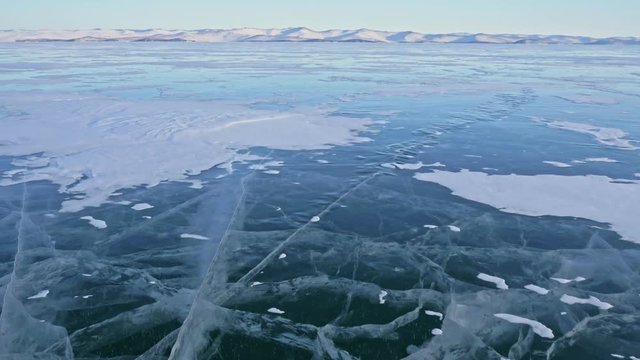 Man and his bicycle on ice. He looks at the beautiful ice in the cracks. First-person view. The cyclist is dressed in a gray down jacket, backpack and helmet. Ice of the frozen Lake Baikal. The tires