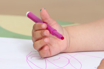 close up on the hand of a child who draws with colored markers