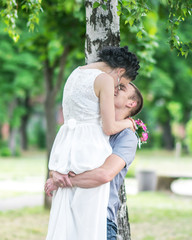 Portrait of beautiful young couple female bride and male bridegroom kissing in summer park. Man husband holding woman wife in his arms. Couple in love. Happy family