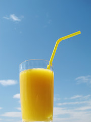 A glass with yellow juice against the blue sky. 