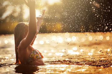 little girl playing in the river. A girl with blond hair raises her hands up in the water and...