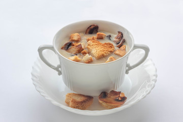 Thick french soup in a mug, heart-shaped toasts and mushrooms on top, white background.