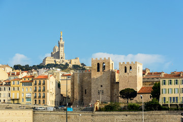 View of the abbey of Saint Victor in Marseille, France, at sunset with its massive fortified square towers, overlooked by the basilica of Notre-Dame de la Garde on top of the hill in the background.