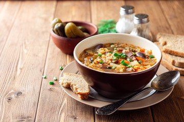 Traditional Russian soup Rassolnik with pickled cucumbers and pearl barley in bowl on wooden table