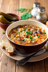 Traditional Russian soup Rassolnik with pickled cucumbers and pearl barley in bowl on wooden table