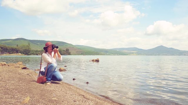Happy beautiful woman hobby photographer taking pictures of nature in front of sea and mountains retro style medium shot