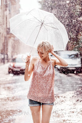 Smiling girl with umbrella posing under rain in street of the city