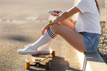 Girl with longboard sit on sidewalk and listening music © Kate