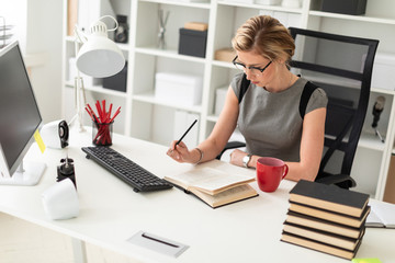 A young girl is sitting at a table in the office, holding a pencil in her hand and reading a book.