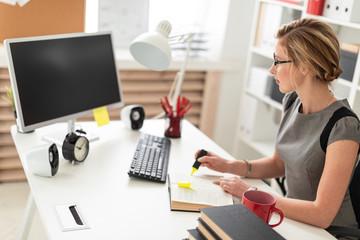 A young girl is sitting at a table in the office, holding a yellow marker in her hand. Before the girl lies an open book.