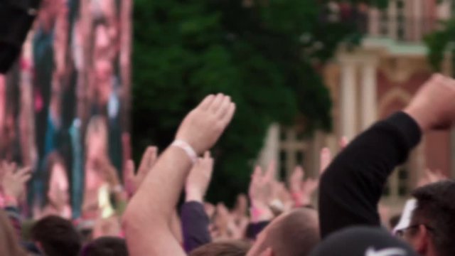 Crowd of young people at a music concert, audience raising hands up. Public event outdoors in a park.