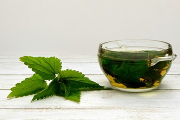 Leaves of young nettle and a decoction in a glass cup on a white background.