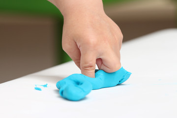 close-up of a child's hand playing with blue and violet modeling clay