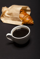 Croissant and cup of coffee on black background